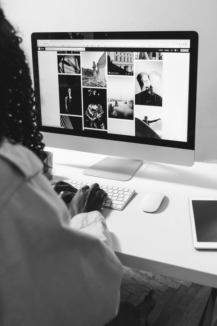 Black and white of crop anonymous African American female working with computer at table with tablet
